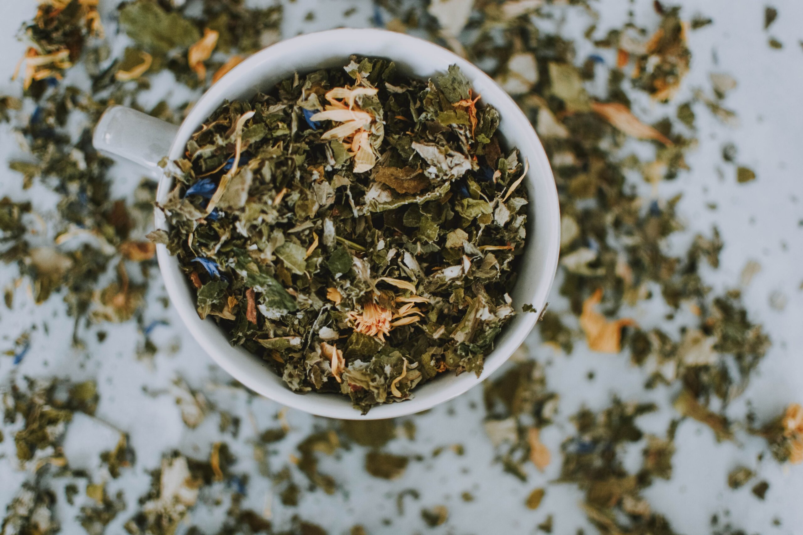 services-01 Overhead shot of a cup with a blend of dried herbal tea leaves and flowers.